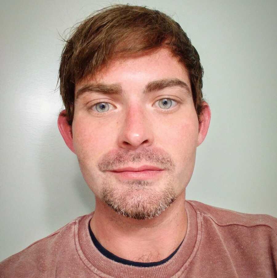 A man with brown hair and light blue eyes wearing a red T-shirt