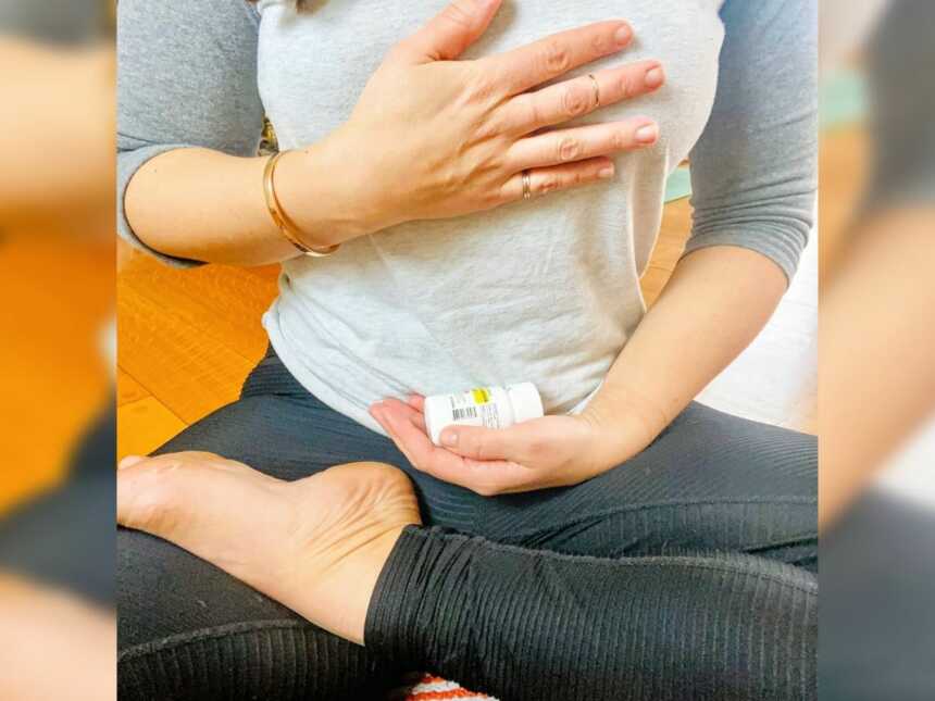 A woman places her hand on her heart while holding a bottle of antidepressants in her lap