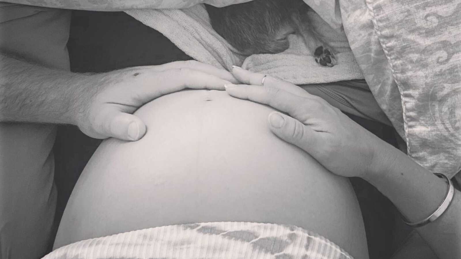Expectant parents place their hands on a mother's exposed pregnant belly