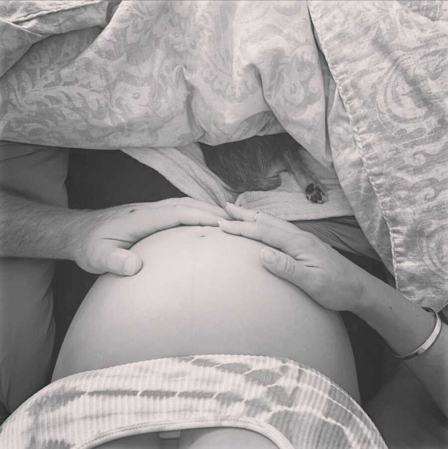 A pregnant woman's belly with two hands resting on it