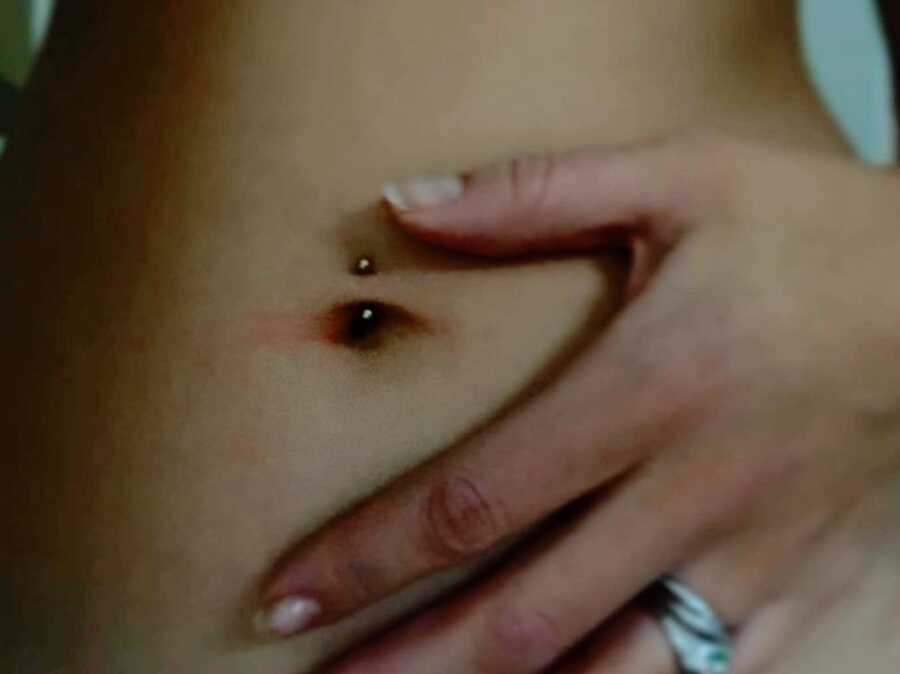 A woman places her hand on her stomach near her pierced belly button