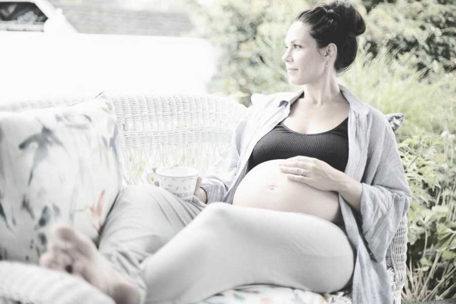 A mom sits on a couch outside with one hand on her pregnant belly