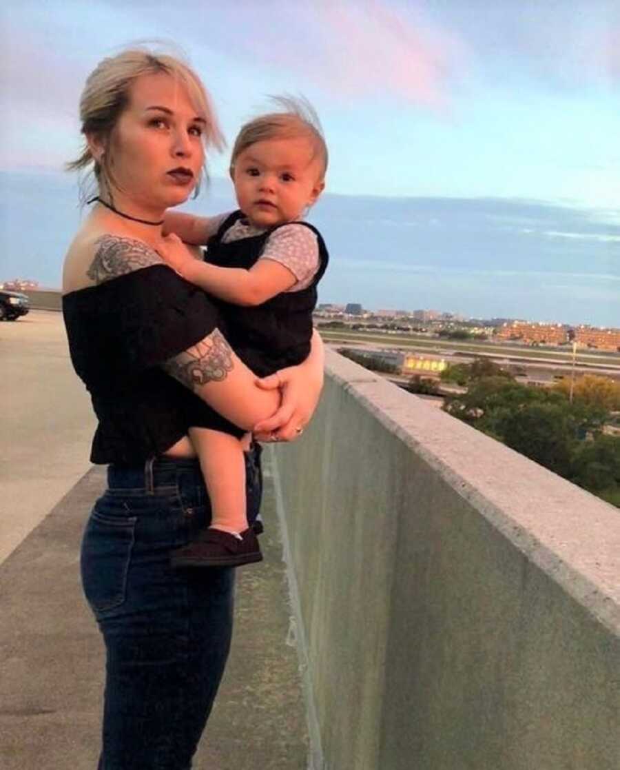 Woman holds her baby and looks off in the distance with a beautiful blue sky behind her.