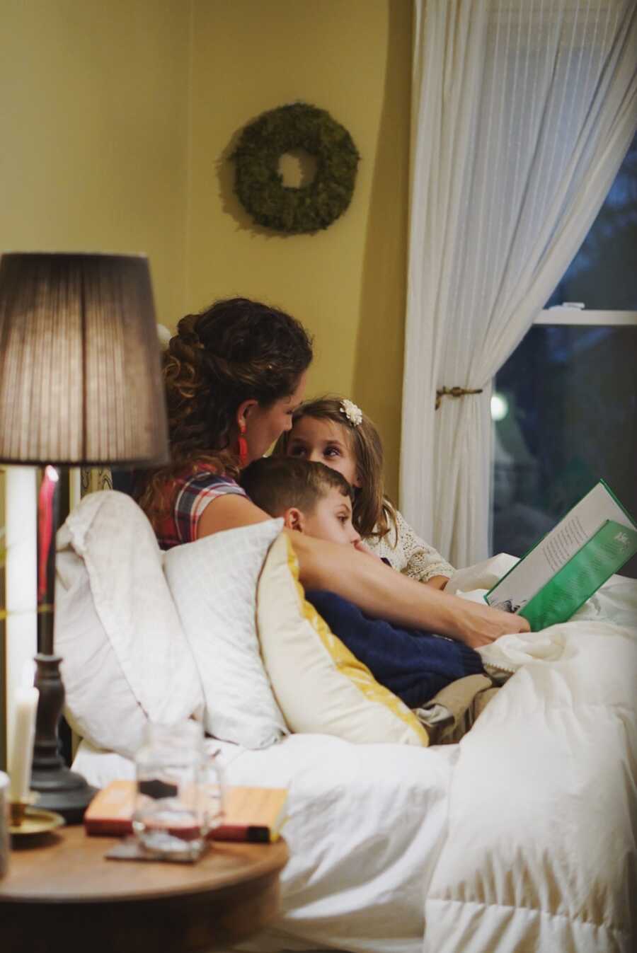 mom sits on couch and reads to her two kids