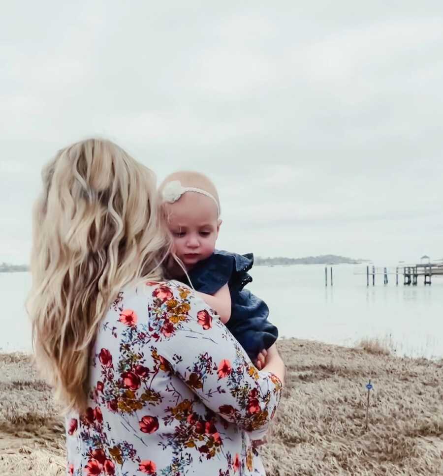 Mother holds her daughter over her shoulder while looking out at water