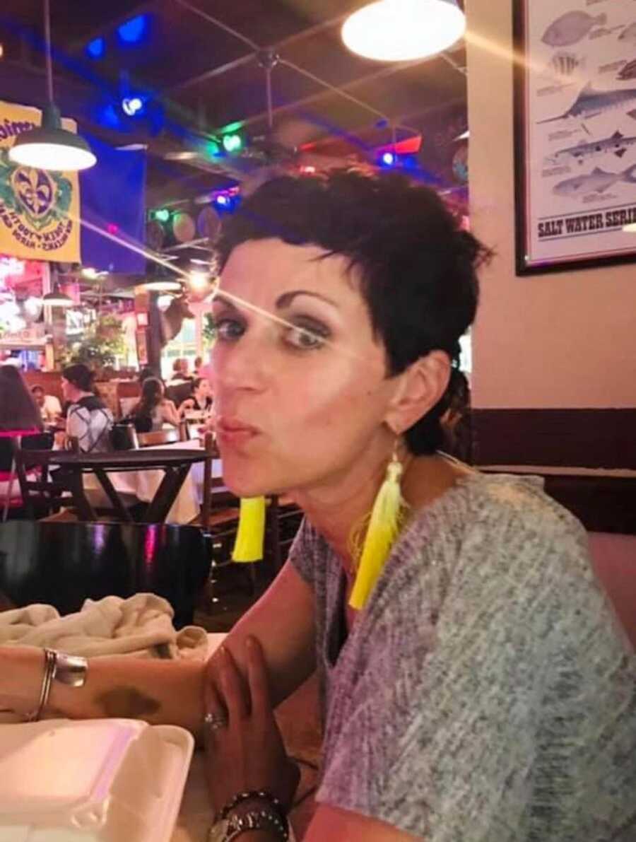 Woman wearing yellow feather earrings sits at a table in a restaurant