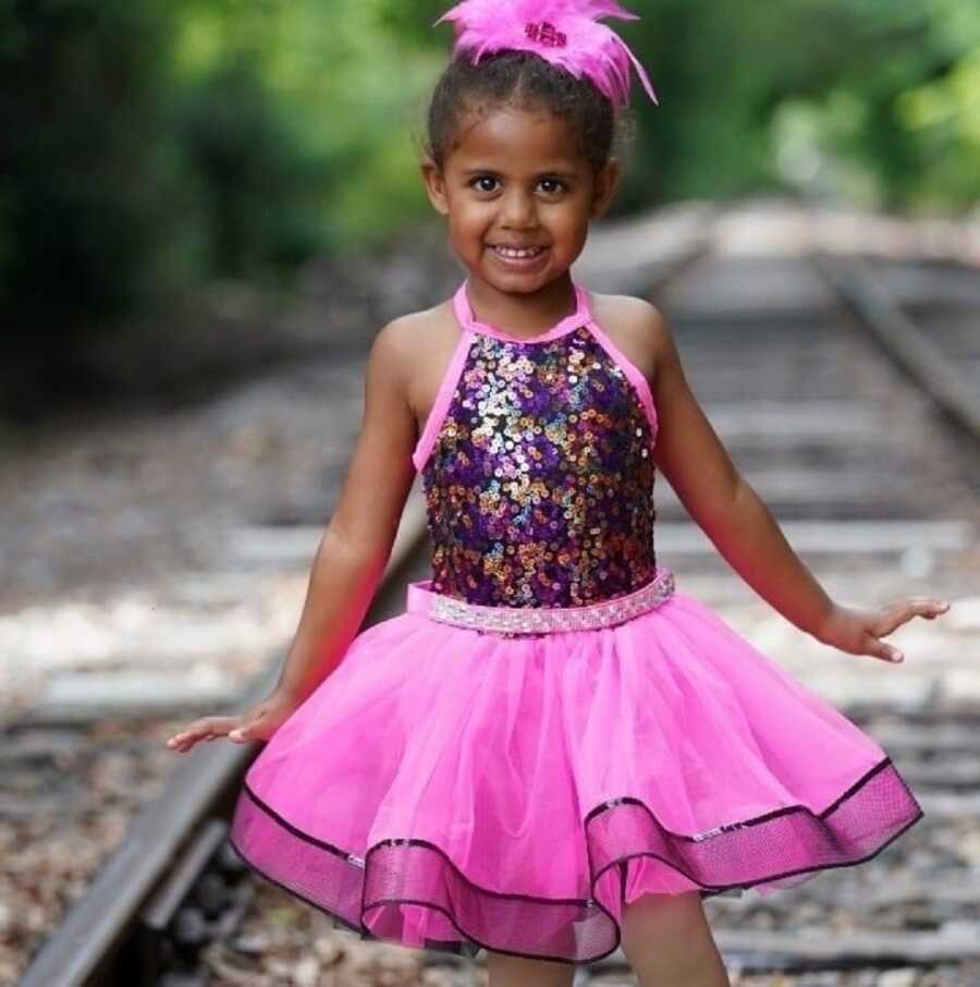 Young black girl takes picture on railroad tracks in sparkly pink tutu dress.