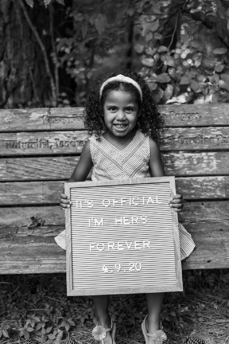 Foster daughter holds up letter board announcing her adoption.
