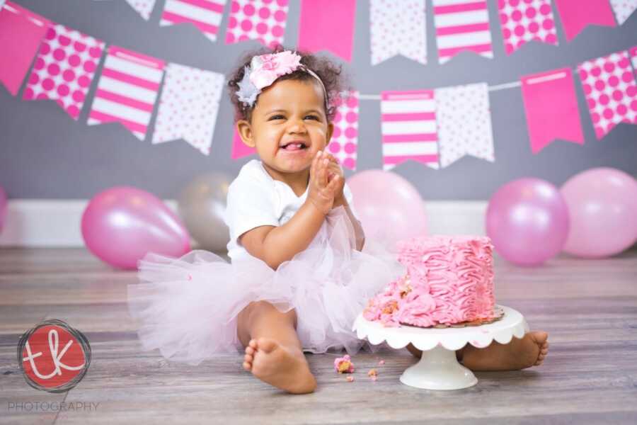 Young black baby girl takes pictures with pink birthday cake and tutu.