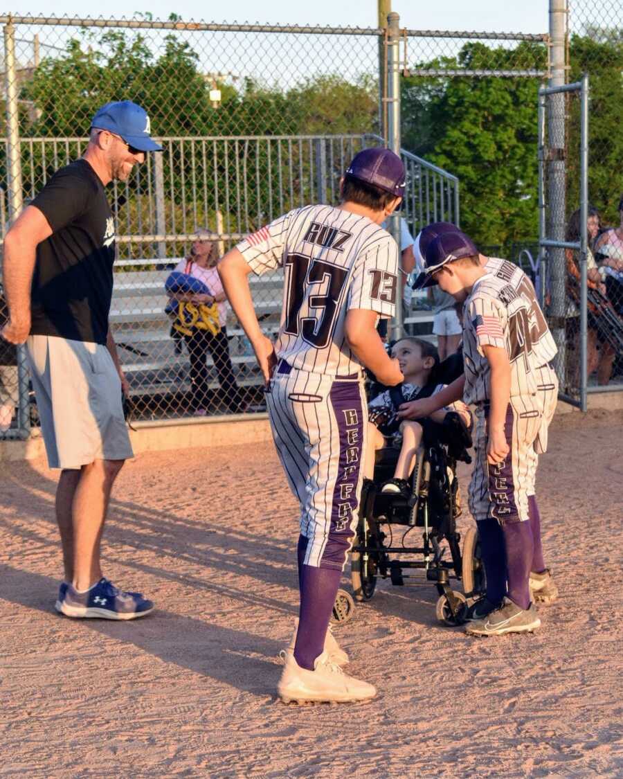 baseball coach and players talk to young boy with physical disability