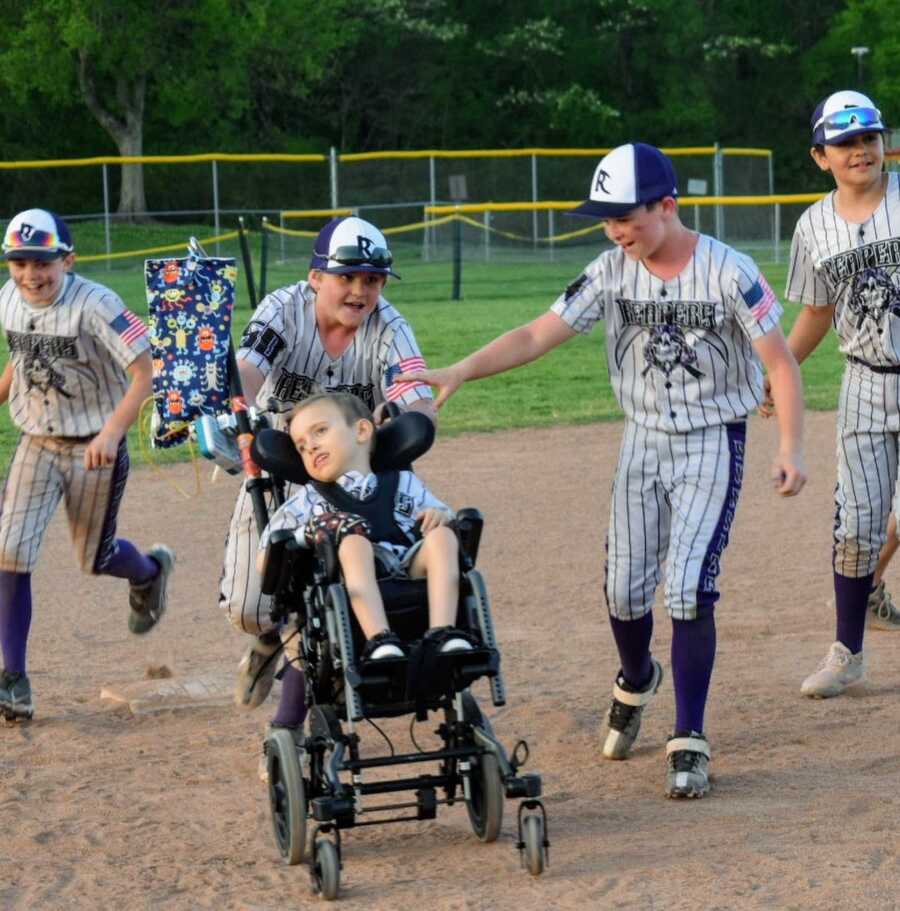 baseball players take boy with disability across the field in his wheel chair