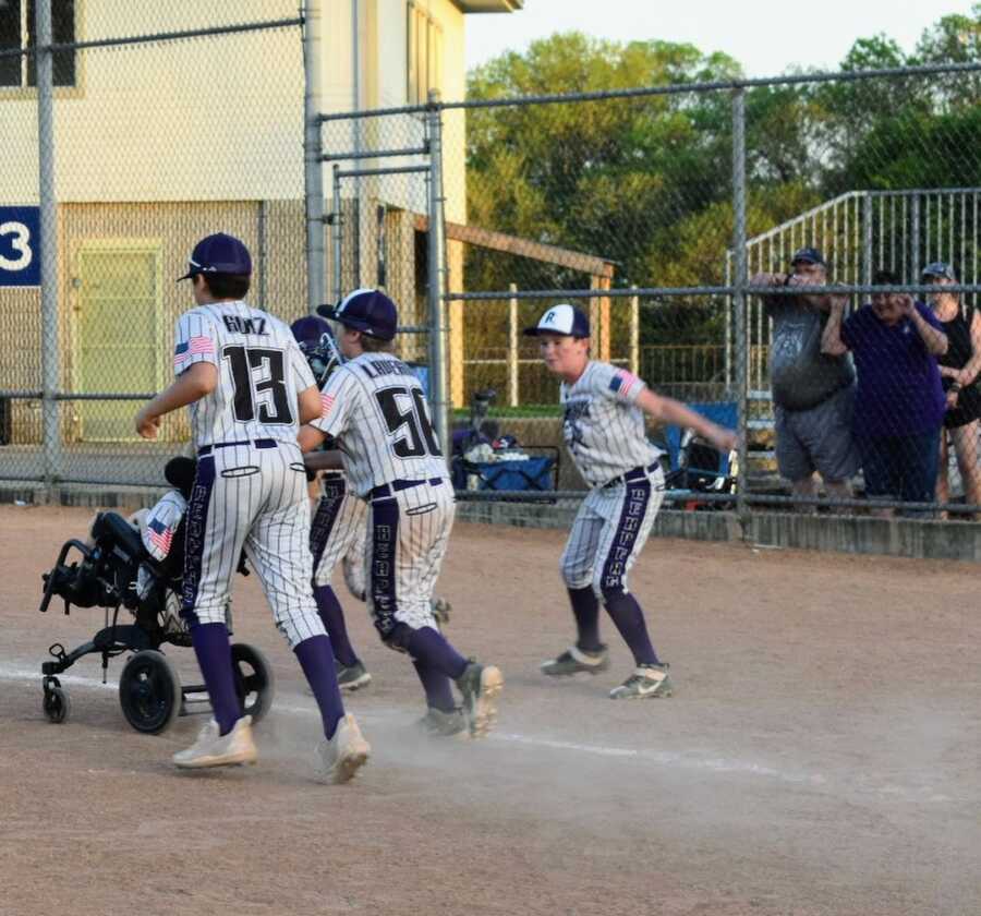 baseball players support boy with disability by running with him on the field