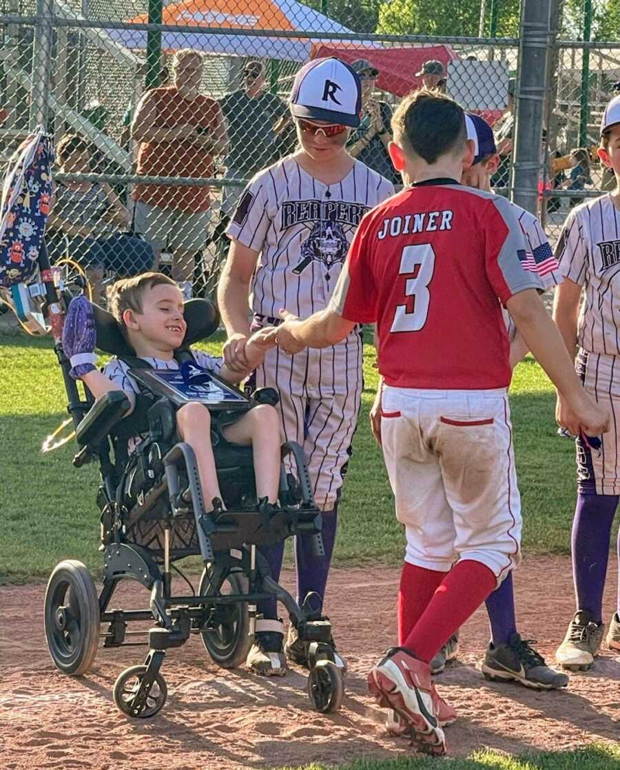 boy with disability sits in line with other baseball players to shake hands with other team