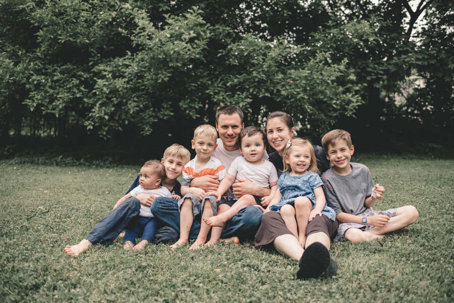 husband and wife sit on grass with bio and adoptive children