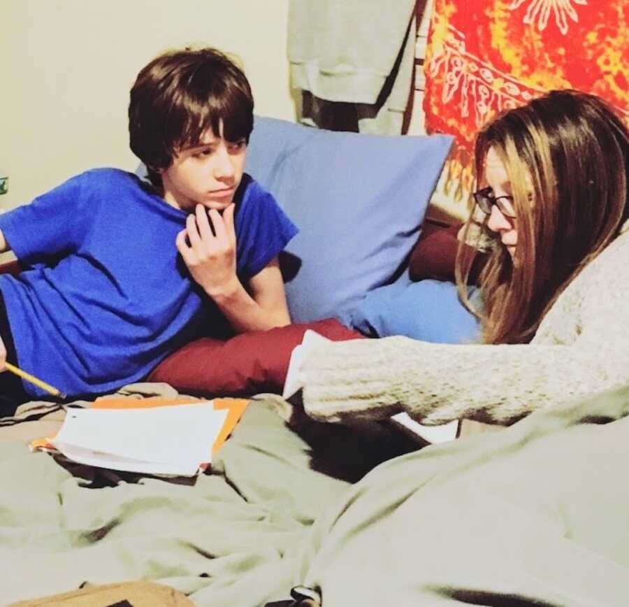 Mother with Lyme disease lays in bed with her son helping him do his homework