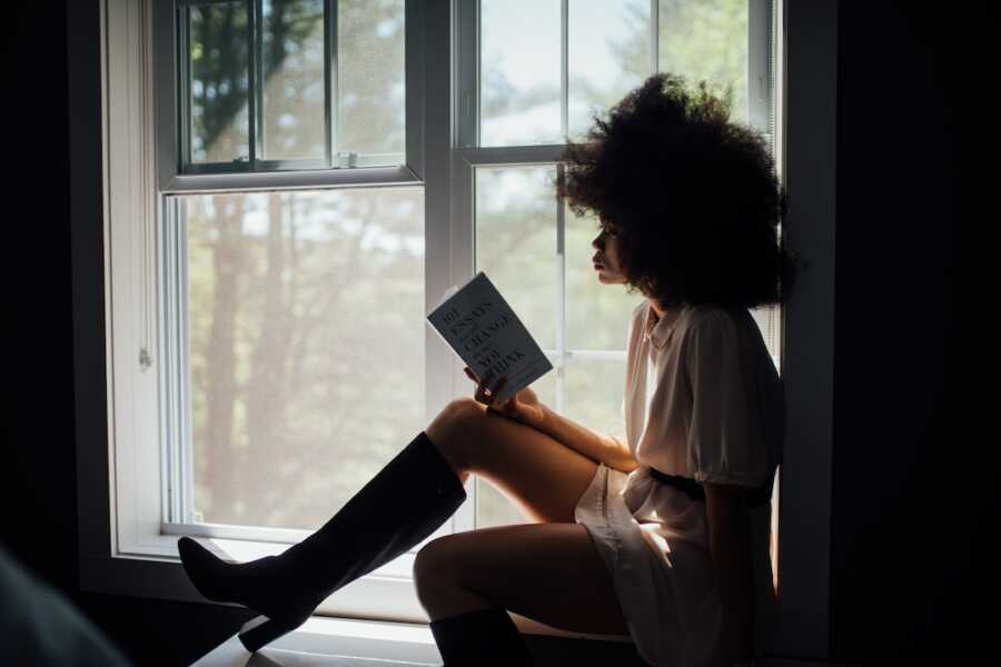 woman sits in window sill reading a book