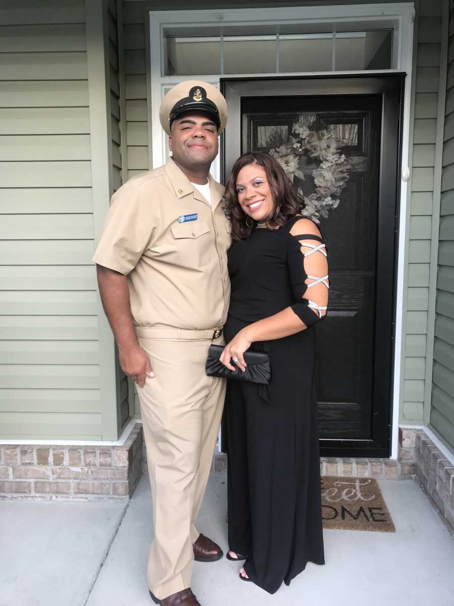 Military couple stand in front of house dressed in uniform and formal black dress.