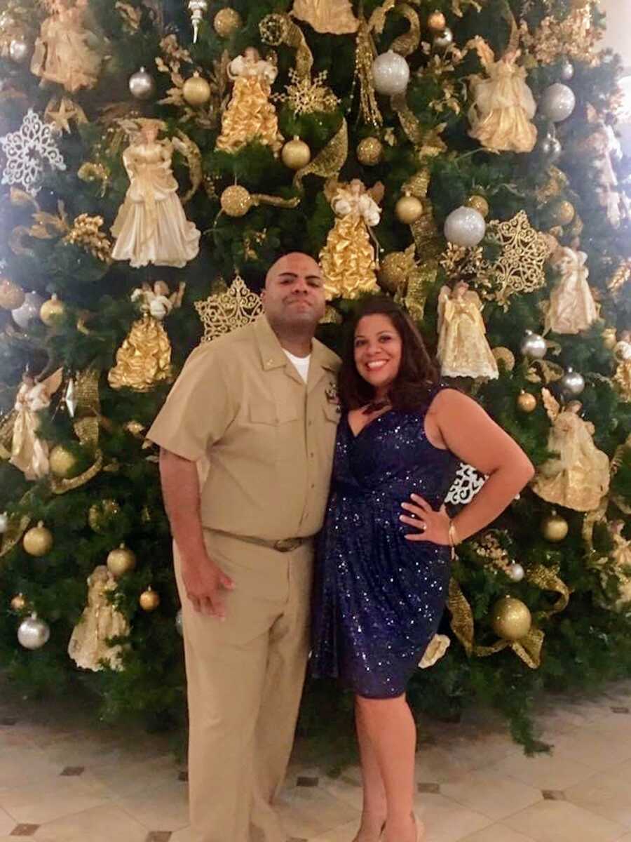 military couple poses in front of a decorated Christmas tree
