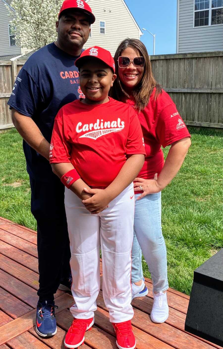parents stand with their son while he is in baseball uniform
