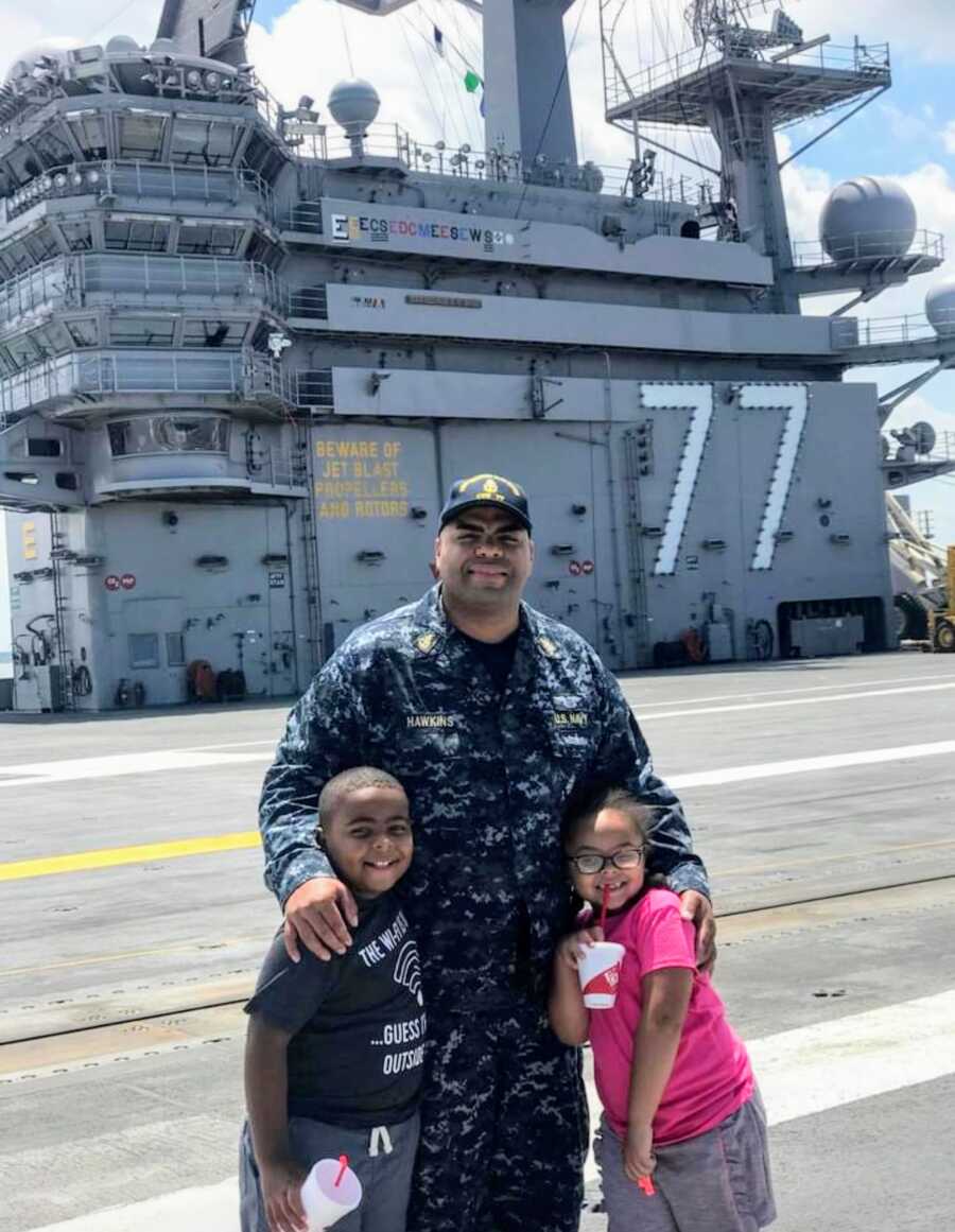 navy dad stands on the ship with his arms around his children
