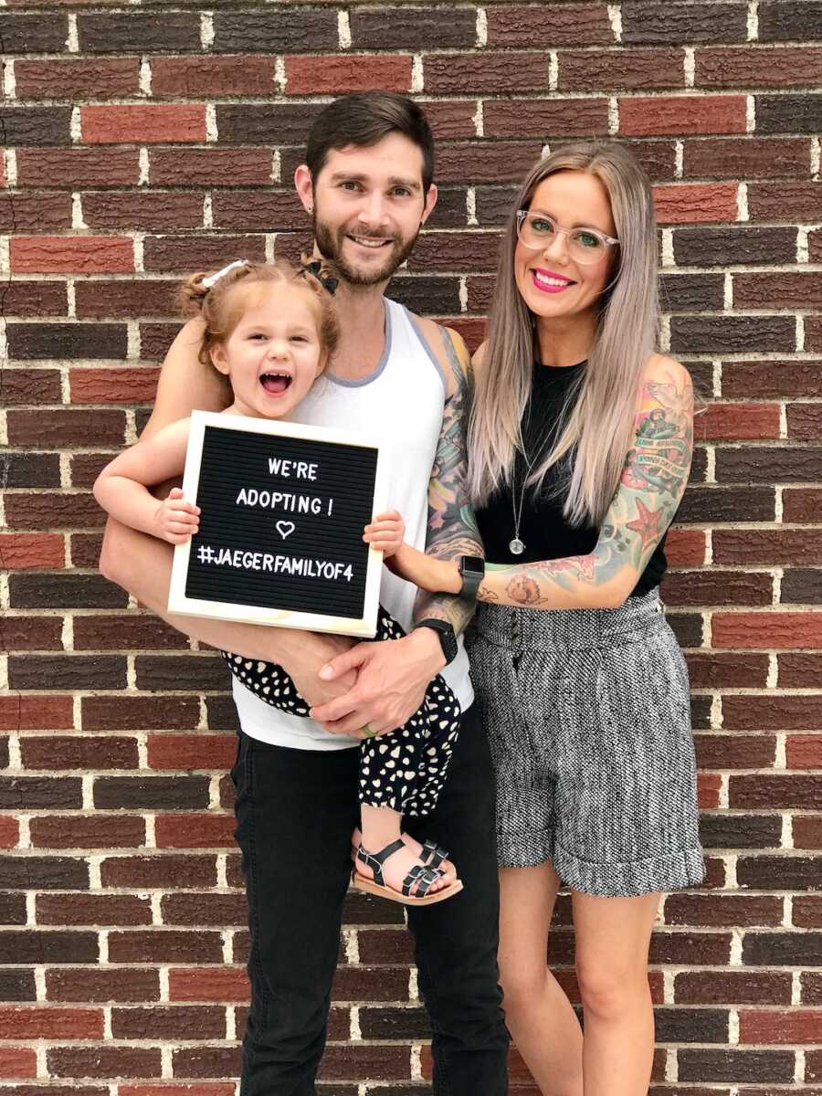 family of three holds sign announcing they are adopting