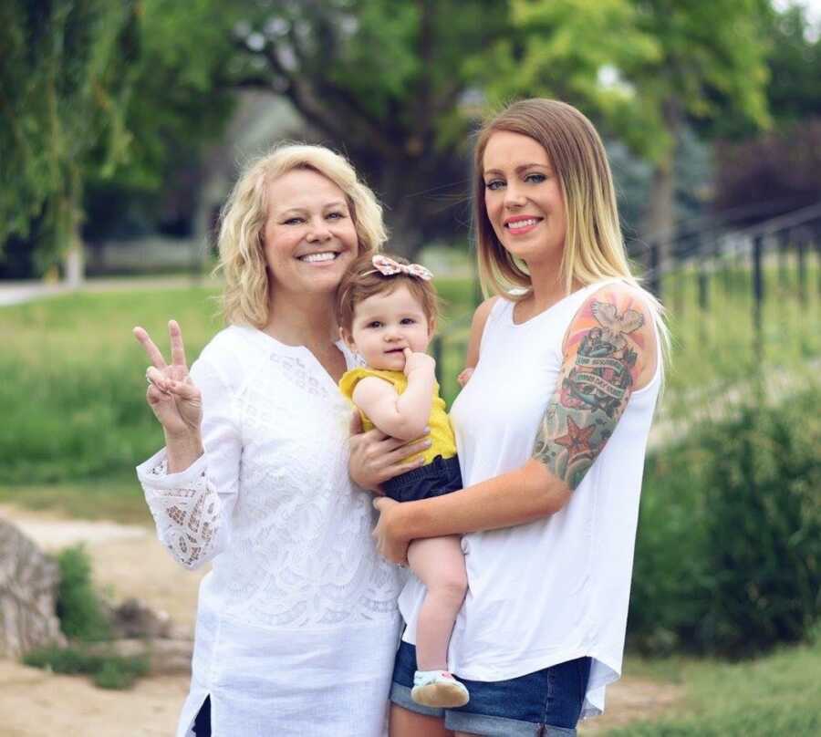 mom stands with her mother and her daughter, smiling