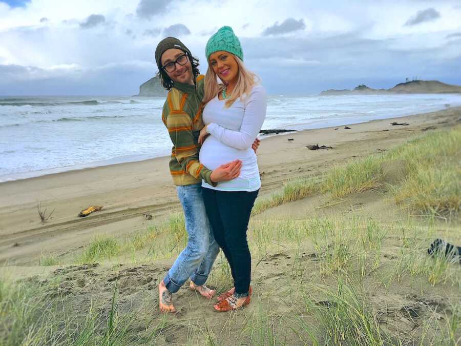 pregnancy announcement of couple standing on the beach