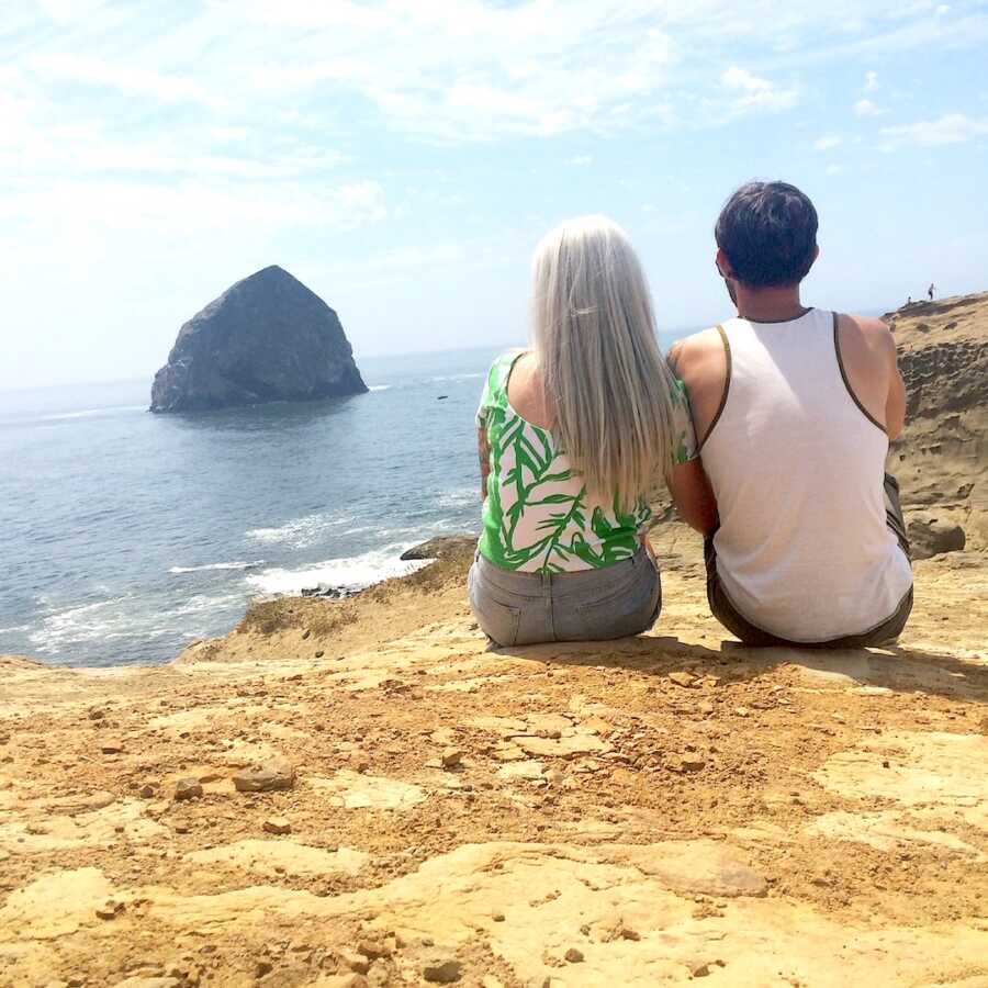 couple sits looking over beach with backs to camera