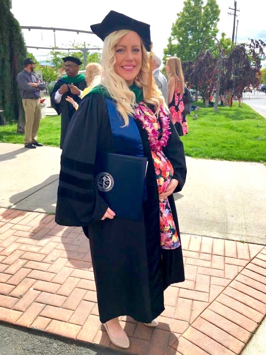 pregnant woman stands in her cap and gown at medical school graduation