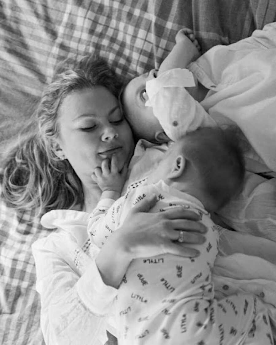 mother laying down on bed with sons in arms