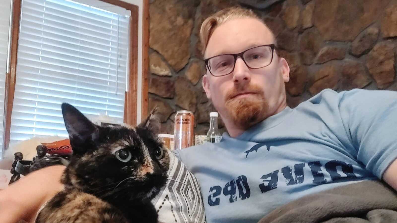 A man sits on the couch with his cat