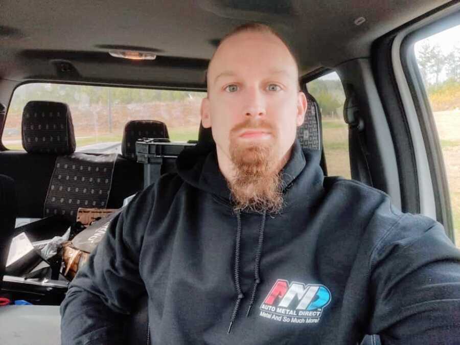 A man sitting in his car wearing a black hoodie