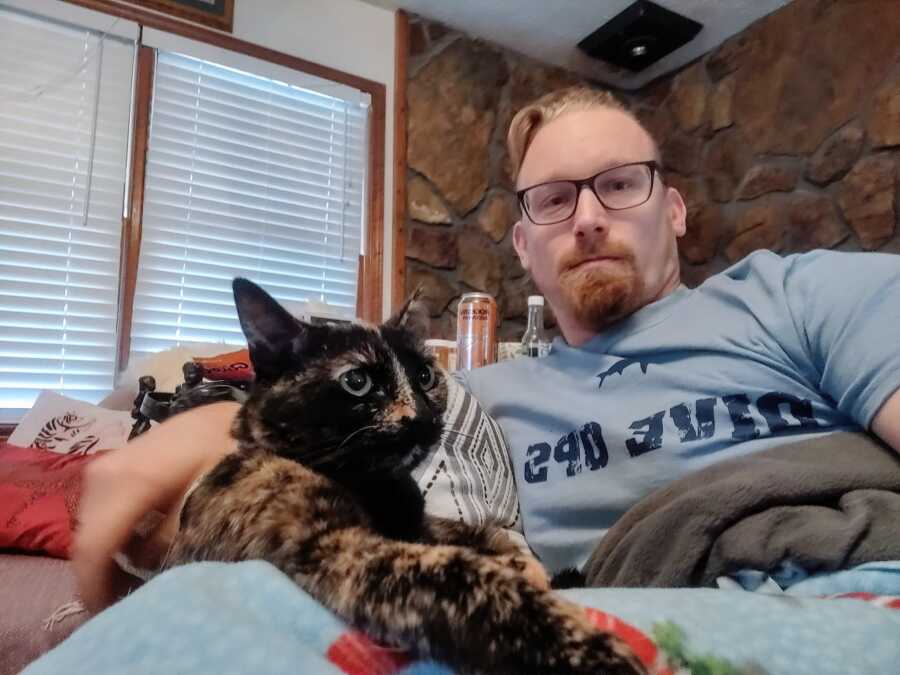 A man sitting on the couch with his cat wearing a grey T-shirt