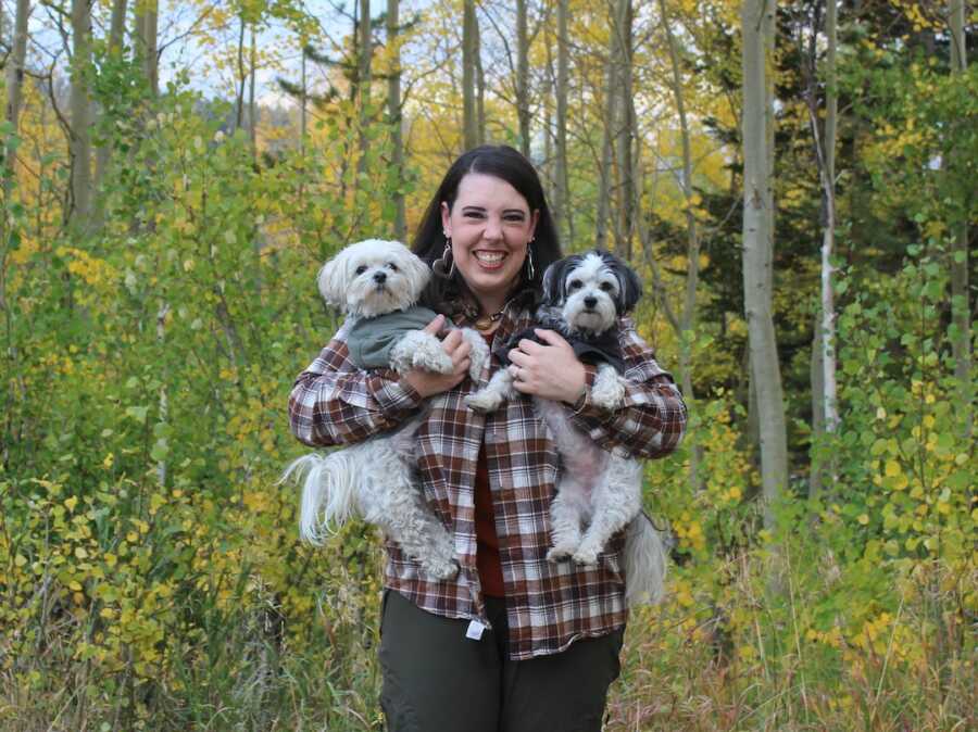 woman with her two dogs in arms smiling in woods