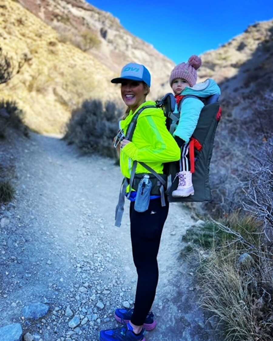 woman on a walk through the mountains with daughter on back 