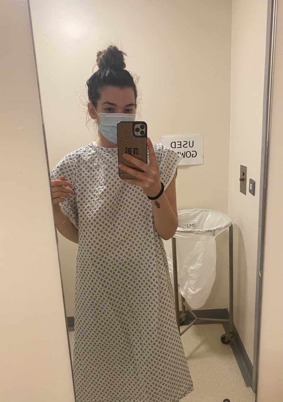 woman standing in mirror in hospital gown 