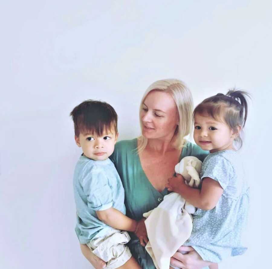 Mom holding her toddler son on her right arm and her toddler daughter on her left one