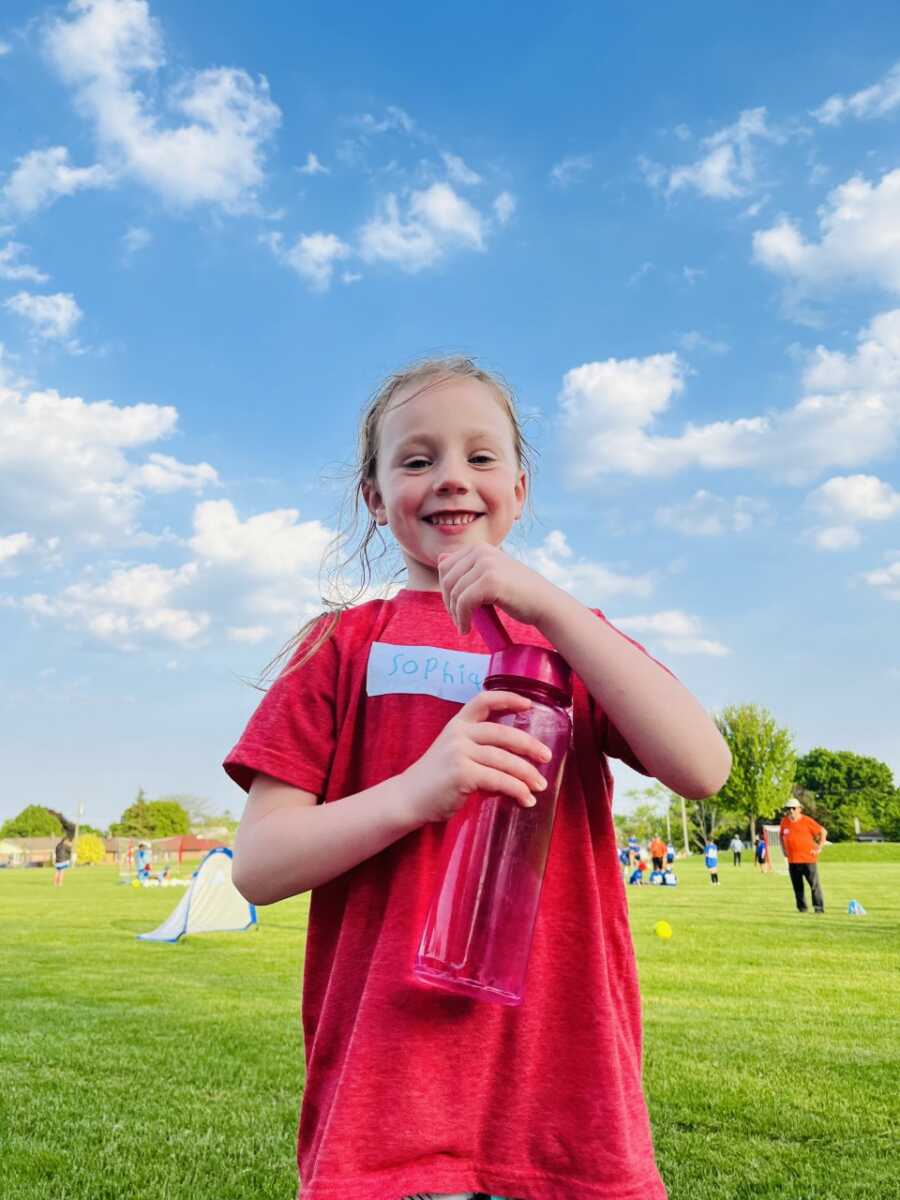Little girl smiles for a photo while playing soccer outside with friends