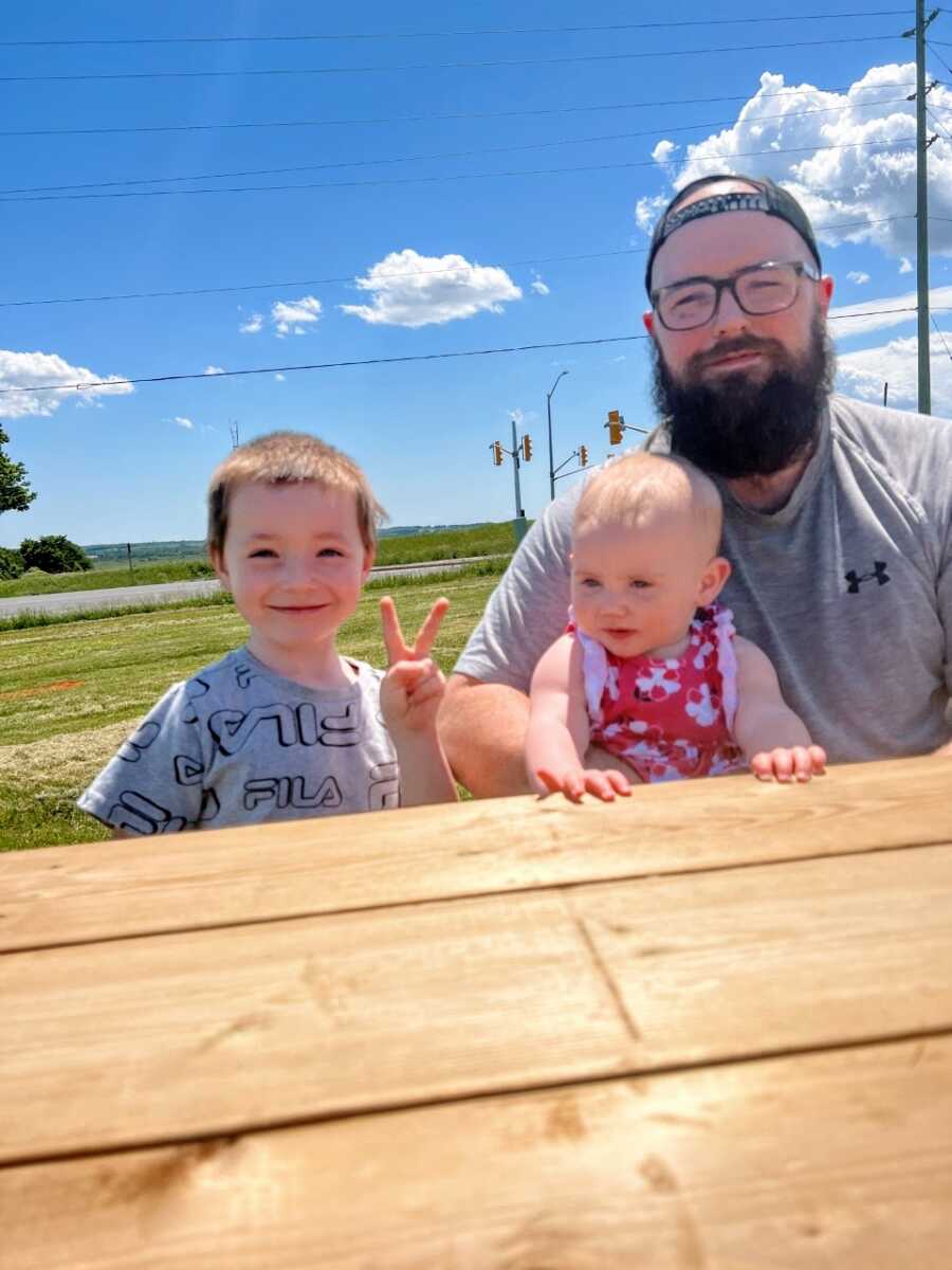 Dad takes a photo with two of his kids while enjoying a sunny day outside