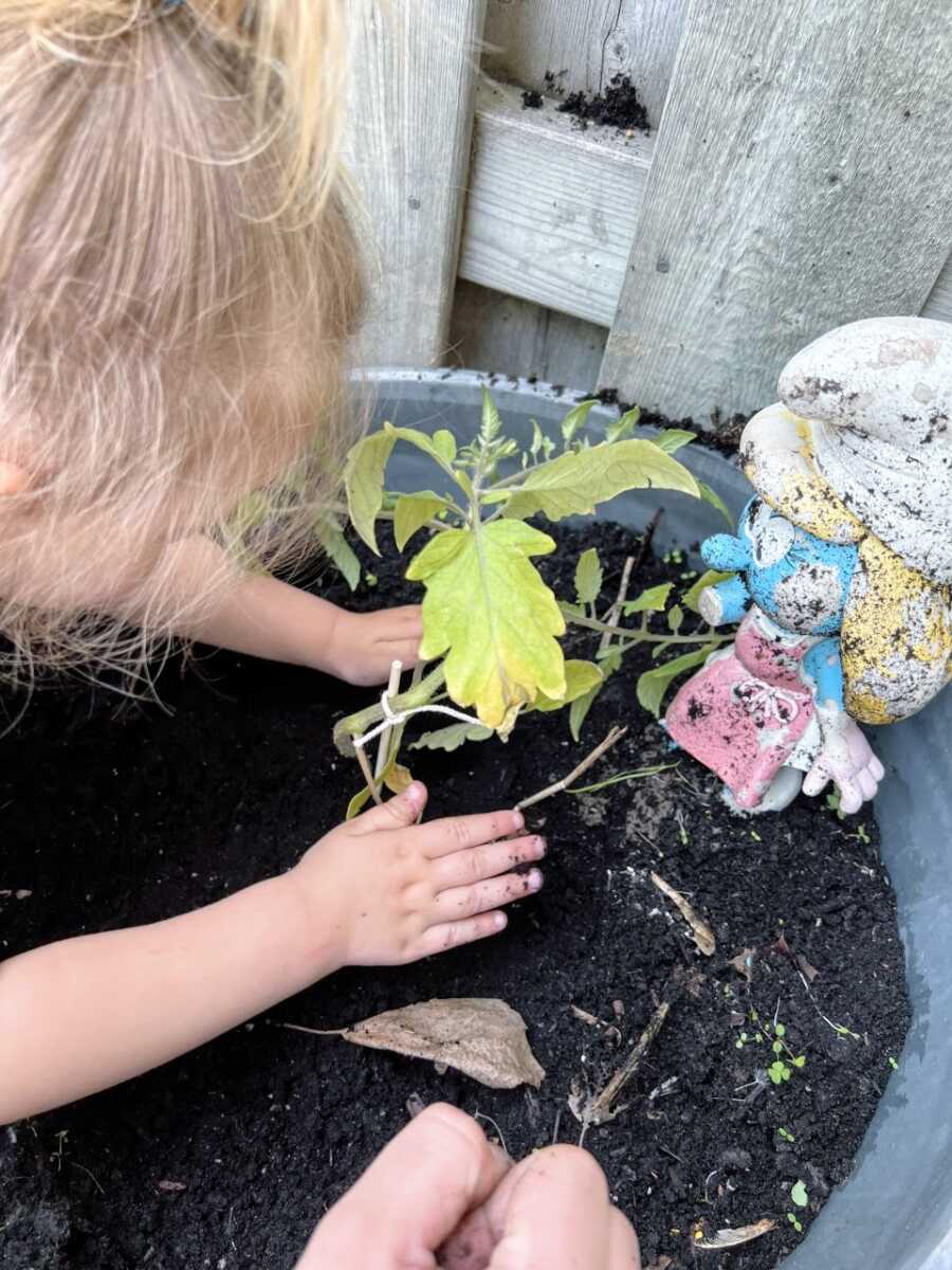 Little girl helps her mom plant some flowers in a pot in their backyard
