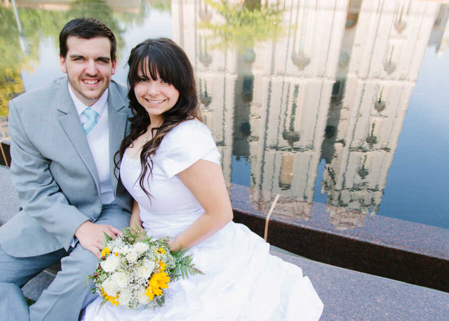 Husband and wife sitting together in front of a public fountain on their wedding day 