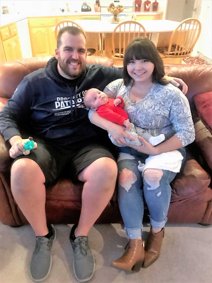 Husband and wife sitting on their couch holding their newborn foster son