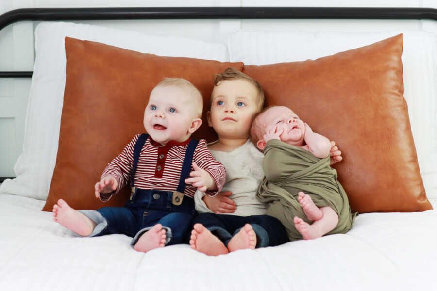Three adoptive baby brothers sitting on a bed resting on a large, leather pillow