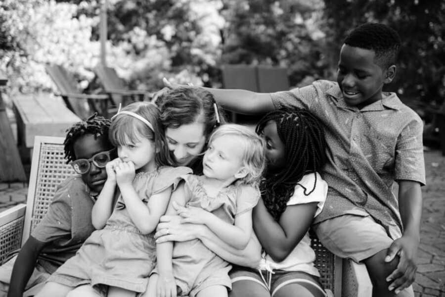 Mom of interracial family takes a photo hugging her five kids while they on sit on a bench outside together