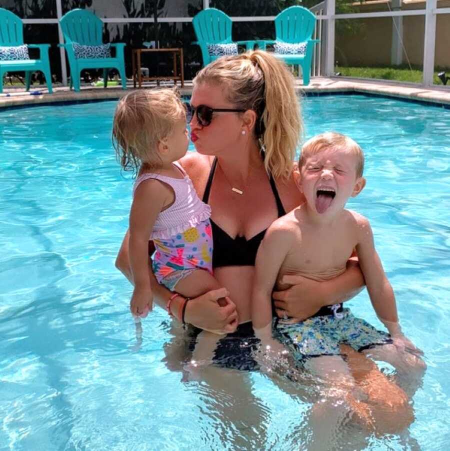 Mom holds her two kids while they all swim in the pool together