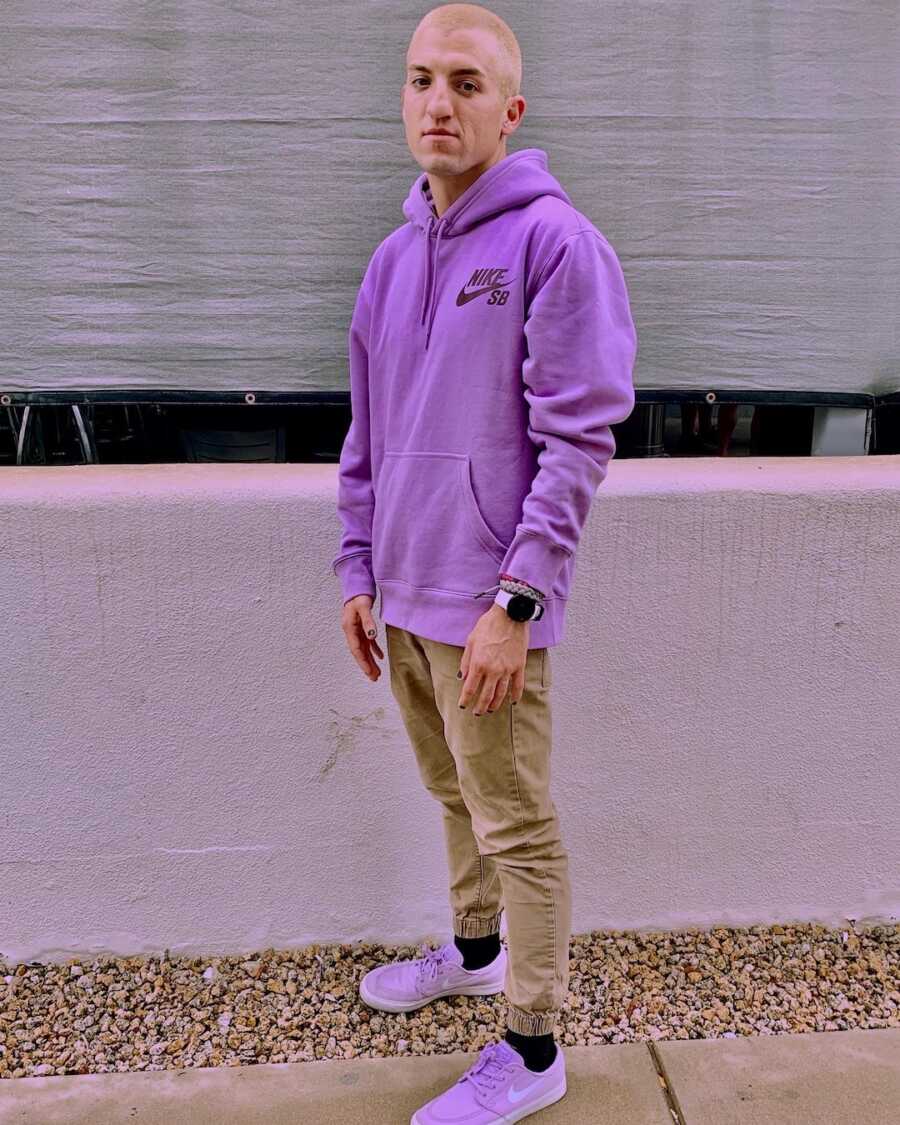 man standing against wall with purple sweatshirt on 