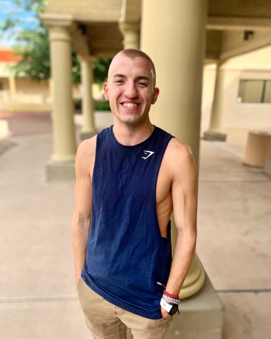 A young man wearing a blue tank top stands by some pillars