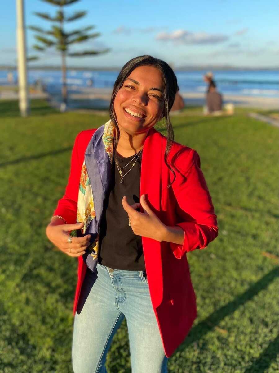 woman standing on grass smiling with hands on jacket 