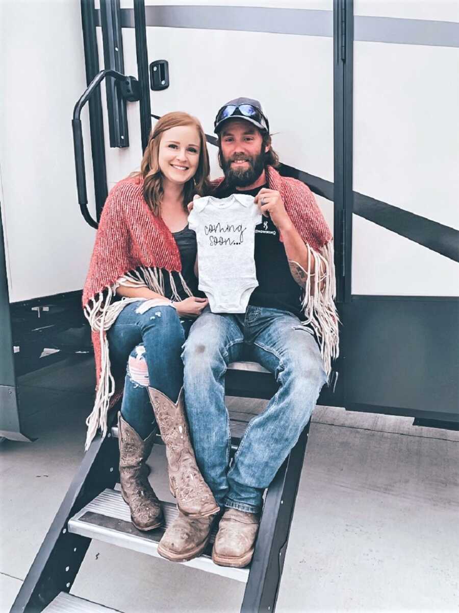 husband and wife holding a onesie that says "coming soon"
