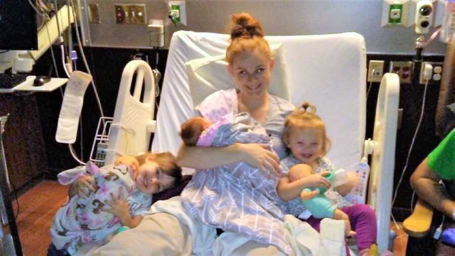 Postpartum mom at a hospital bed with her two little daughters holding her newborn baby